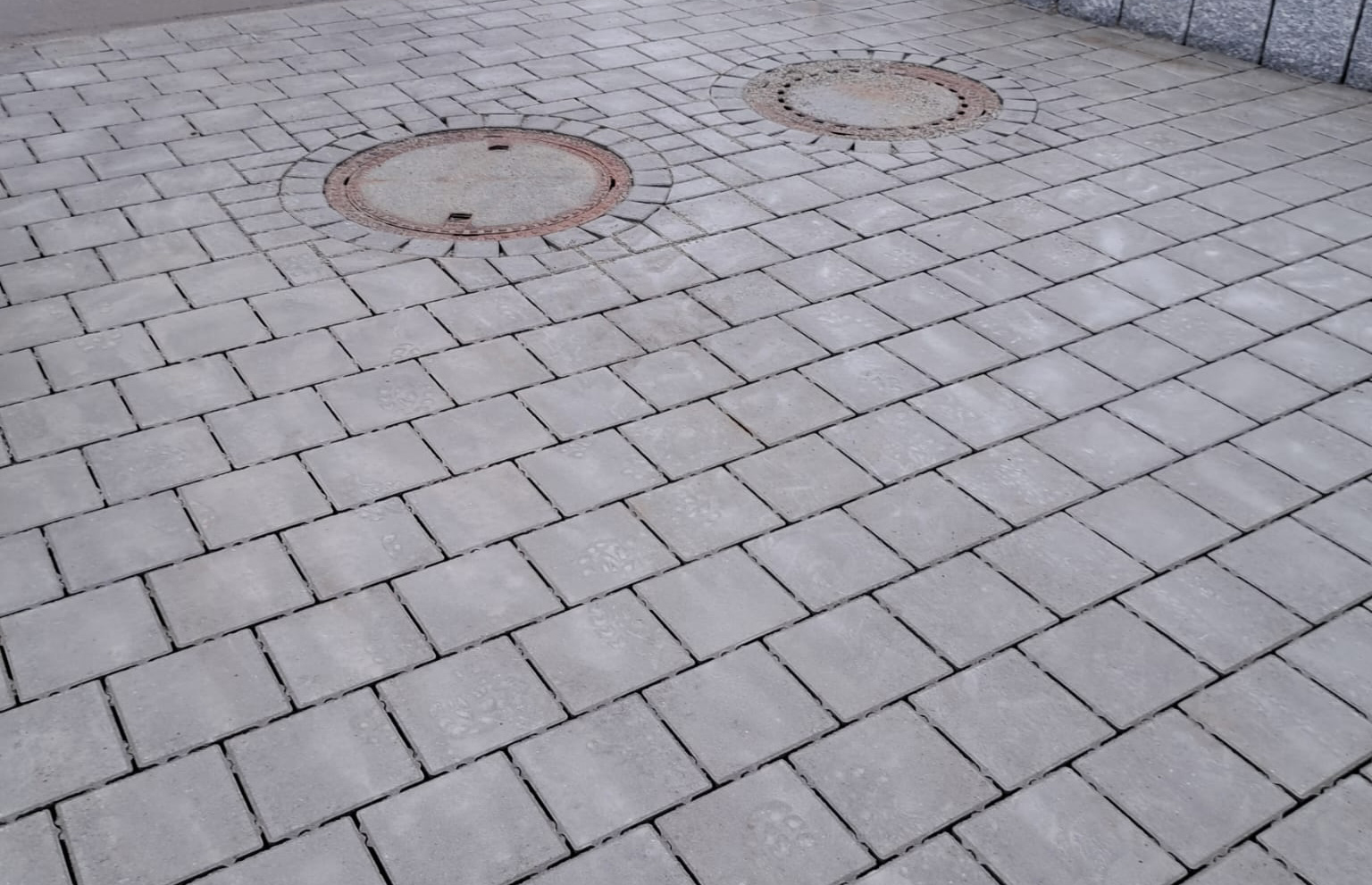 Verlegung von Pflaster und Schachtabdeckung mit Natursteinen integriert.
